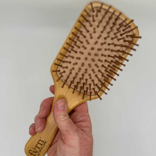 Wooden hairbrush held by a hand against a plain background