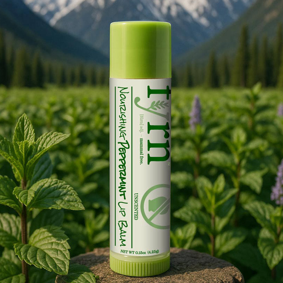 Lip balm tube with green lid and label against a natural background with plants and mountains.