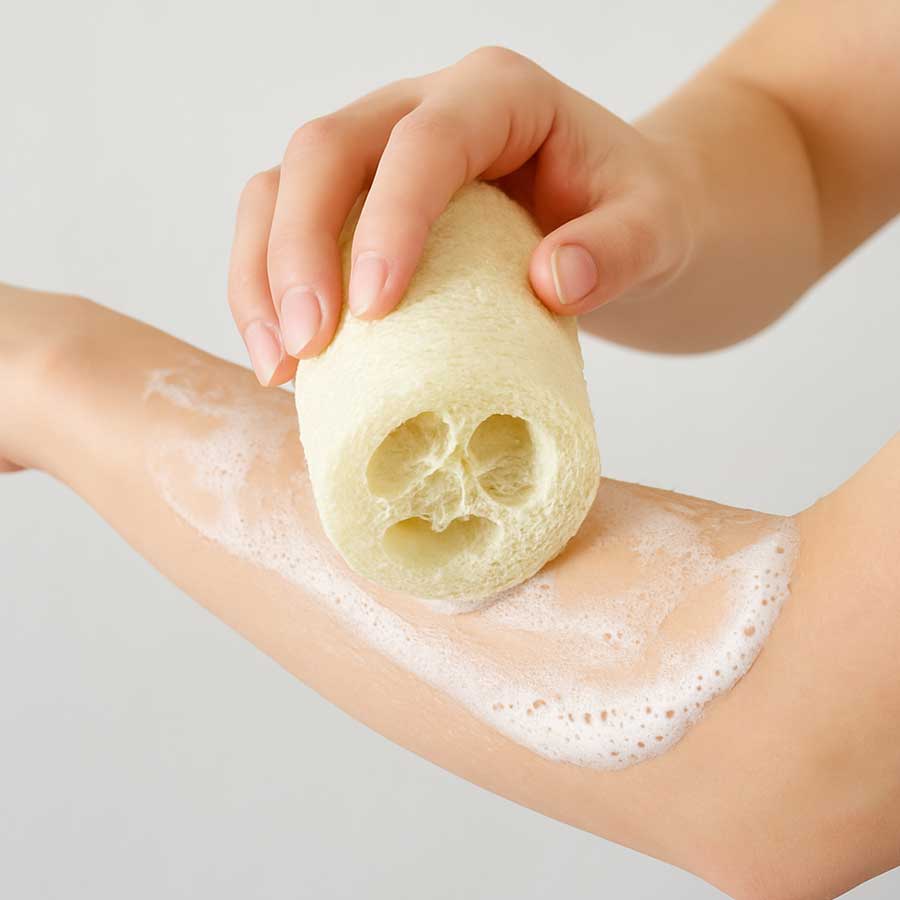 Hand using a loofah sponge on a person's arm with soap suds.