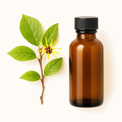 Brown glass bottle with black cap next to a branch with leaves and a yellow flower on a white background